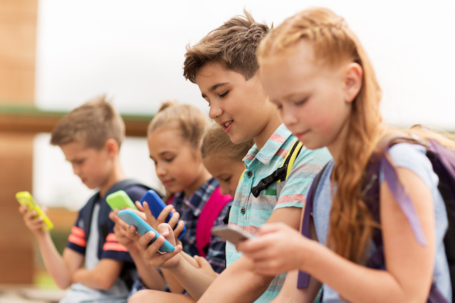This is a picture of kids using smartphones. Prolonged computer and smartphone usage can lead to bad posture where the head and shoulders are draw forward called tech neck. This article is about how to fix tech neck.